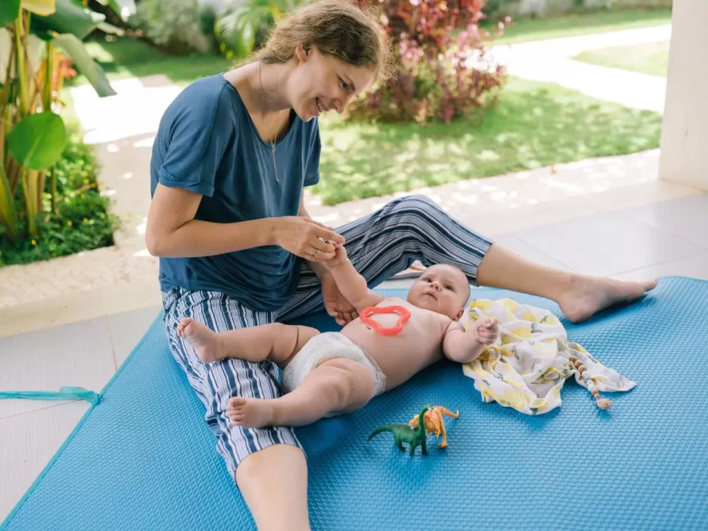 Mom teaching her baby sign language. Baby is lying on a blue mat. 