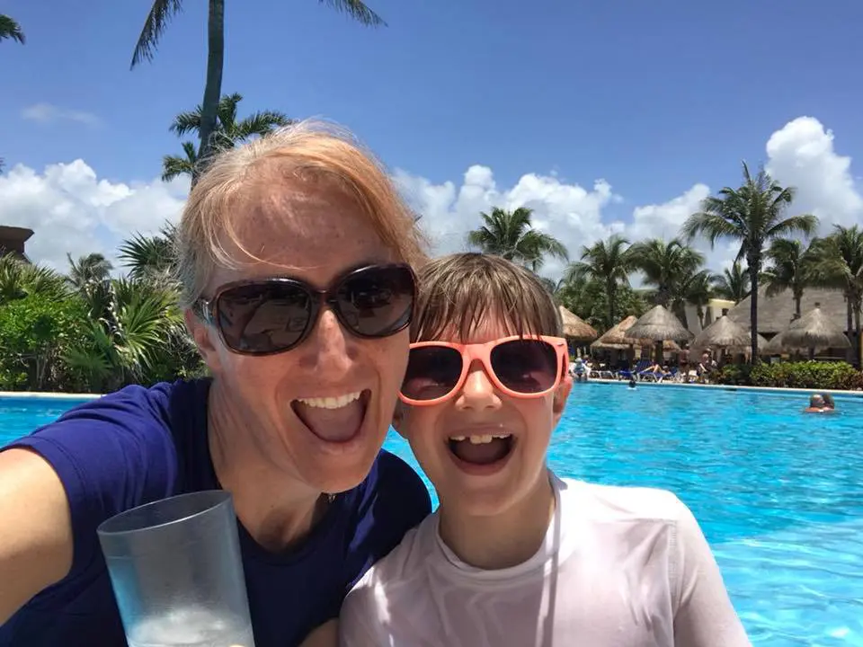 A mom and son wearing sunglasses at a pool smiling at the camera. Solo parent travel