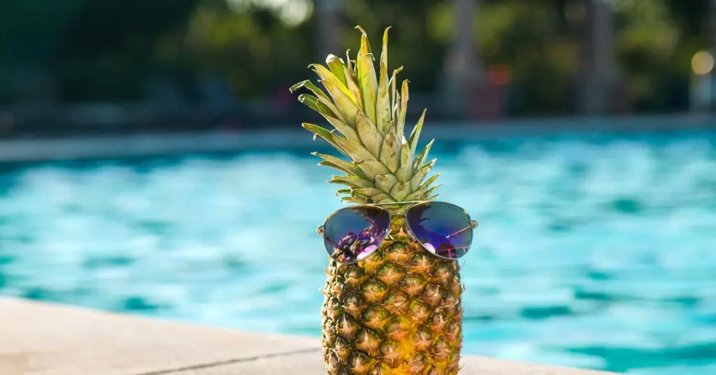 Pineapple with sunglass in front of a swimming pool