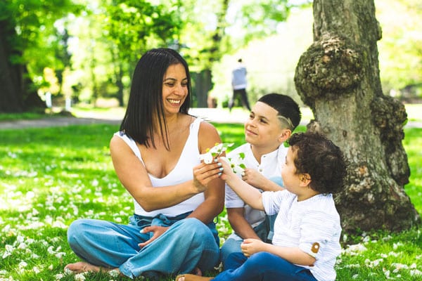 Mom at the part with two kids sitting in the grass in front of a tree