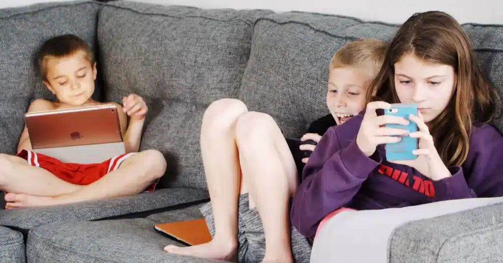 three children on a couch with phones and tablets