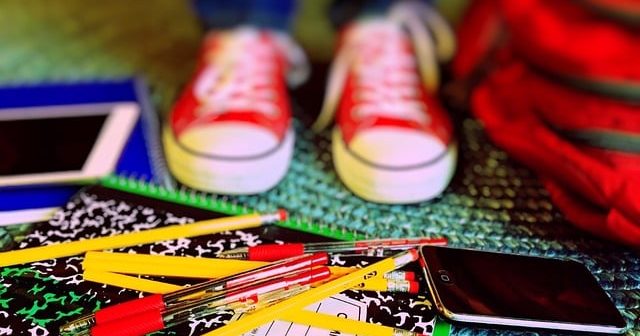 An image of a child's feet wearing red converse shoes, with pencils and a schoolbag on the floor.