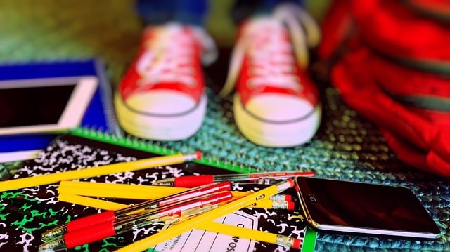 An image of a child's feet wearing red converse shoes, with pencils and a schoolbag on the floor.