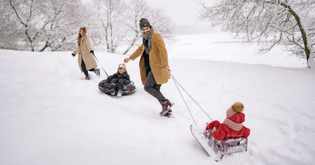 Family playing in snow with kids on sleds