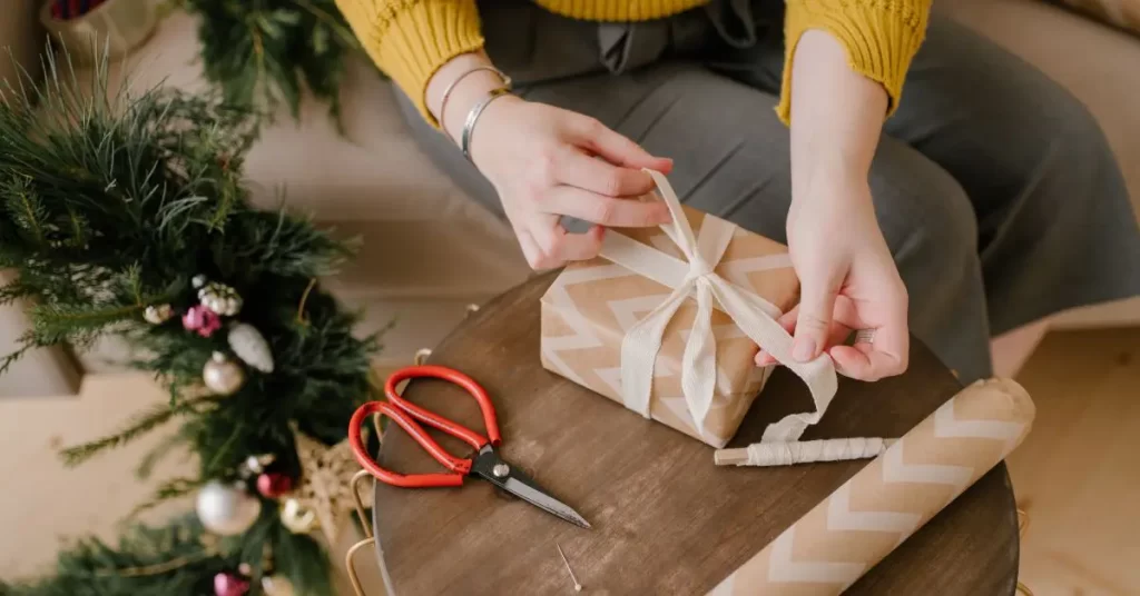 person wrapping a gift with brown paper and red scissors beside the gift