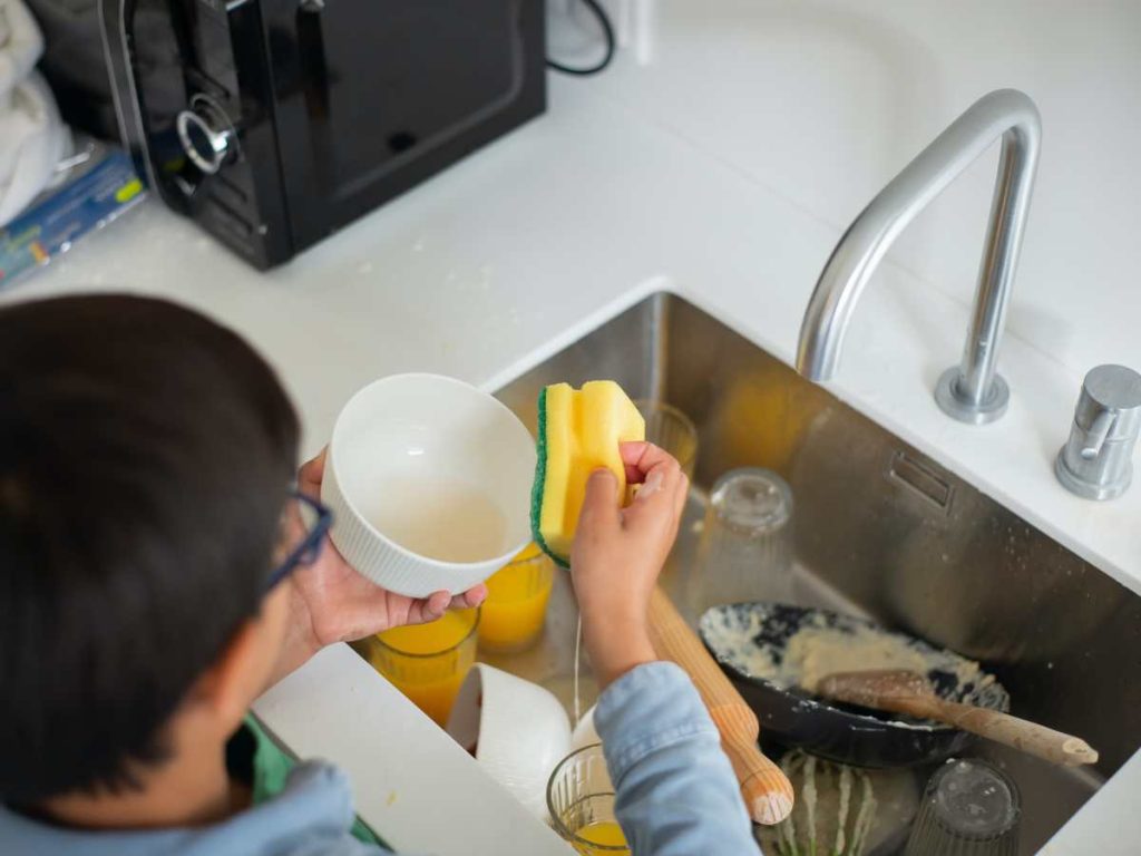 child cleaning dishes at the kitchen sink