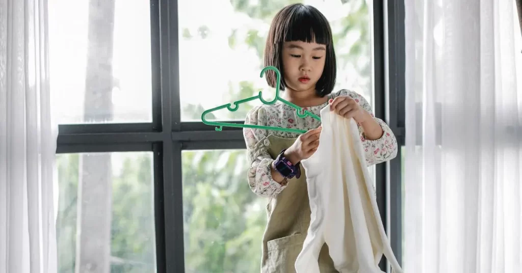 child doing chores by hanging clothes on a hanger