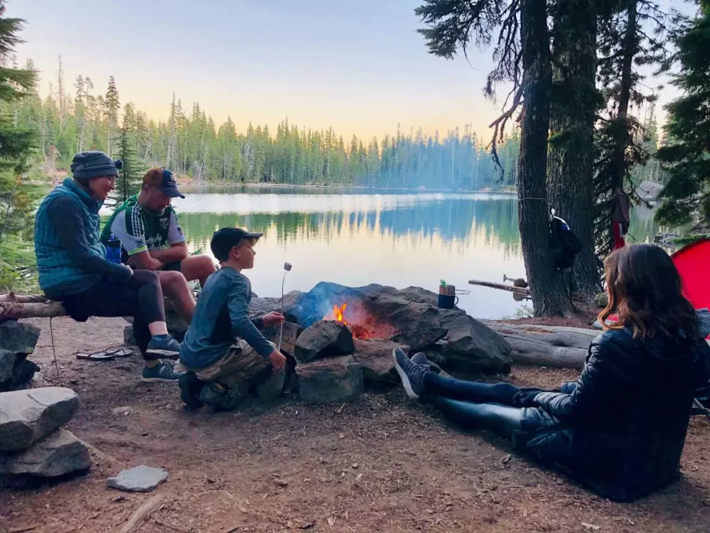 Parents take children camping at a lake sitting in front of a fire