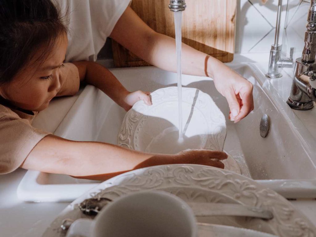 girl washing dishes with mom