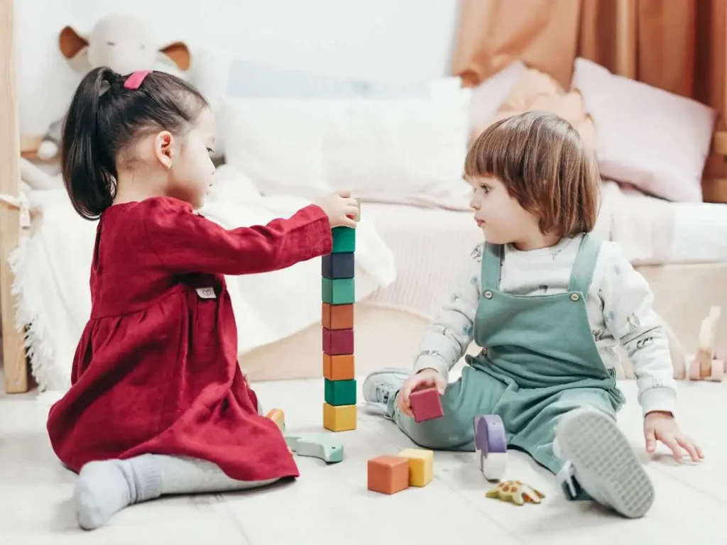 two kids sitting on the floor and playing with lego blocks