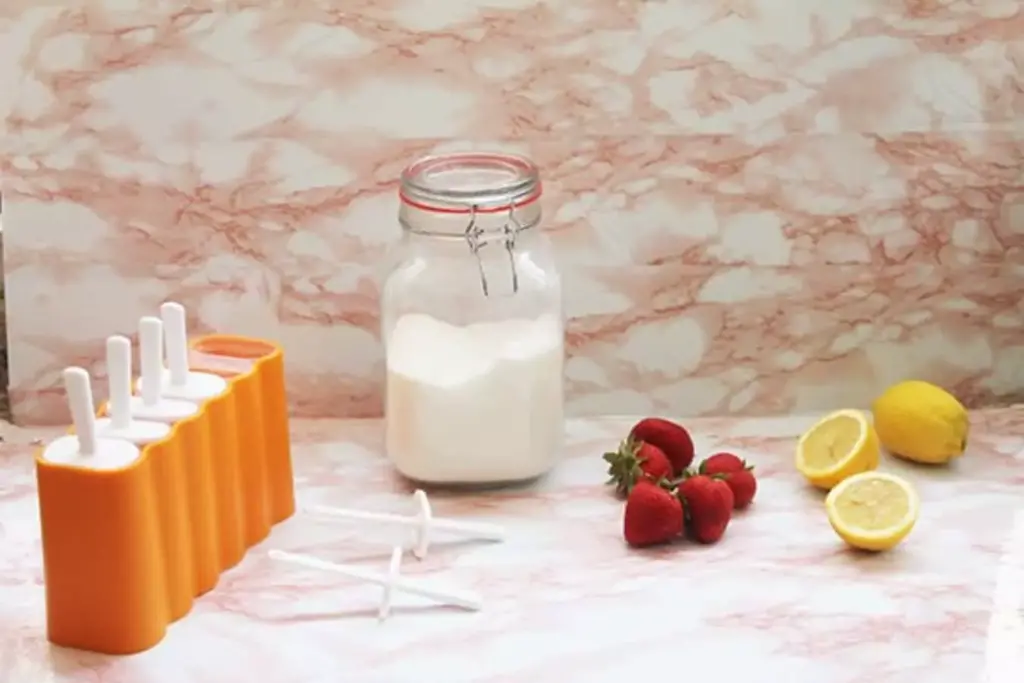 ingredients for a strawberry lemonade popsicle on a table. Lemons, strawberry, popsicle mold seen in picture