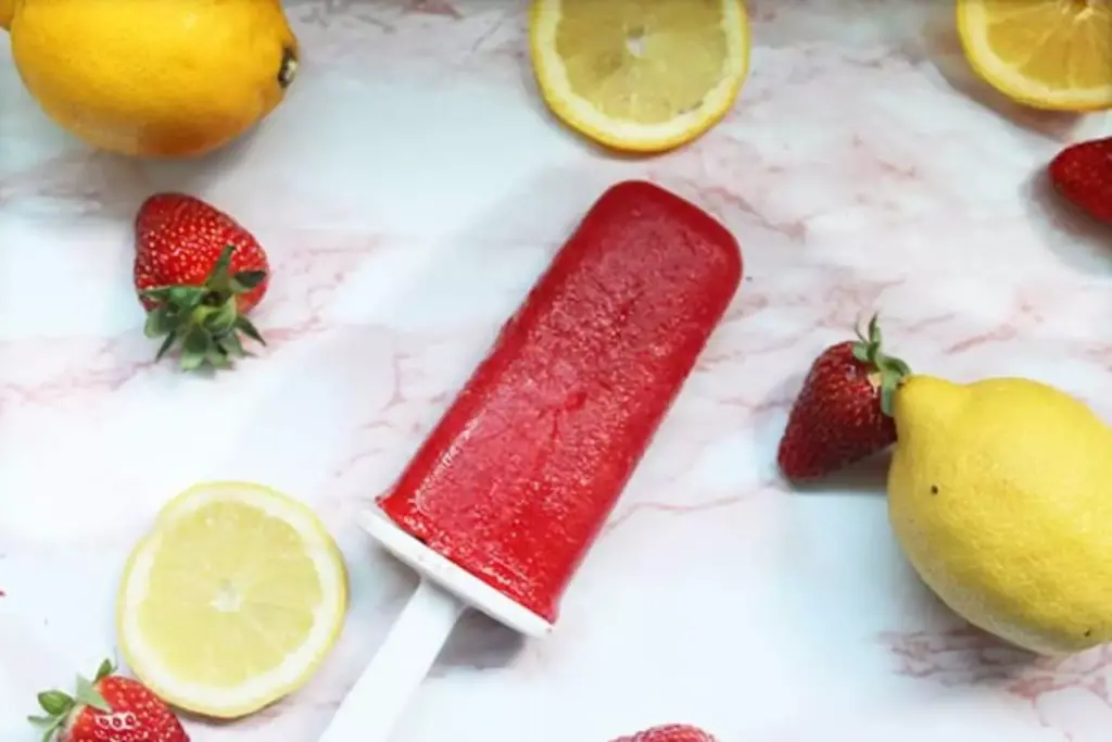 strawberry lemonade popsicle seen in picture surrounded by lemons and strawberries