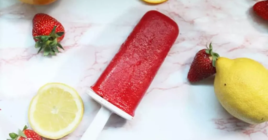 strawberry lemonade popsicle seen in picture surrounded by lemons and strawberries